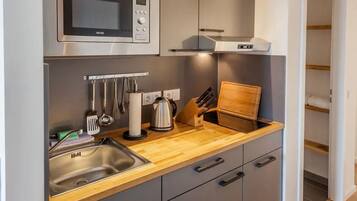Una cocina compacta con microondas de acero inoxidable, hervidor y tabla de cortar de madera.