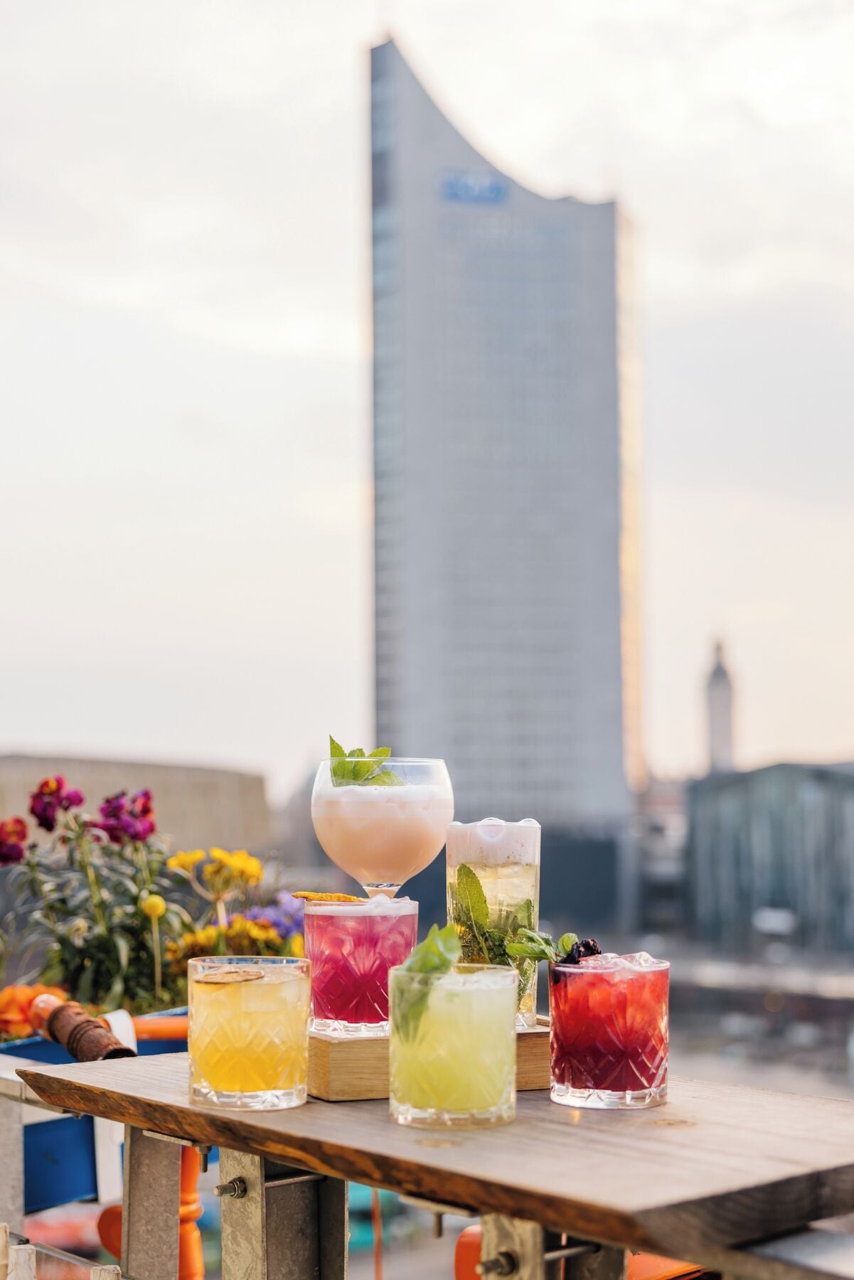 A variety of colorful cocktails on a table with a city skyline in the background.