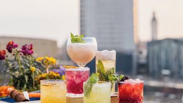 A variety of colorful cocktails on a table with a city skyline in the background.