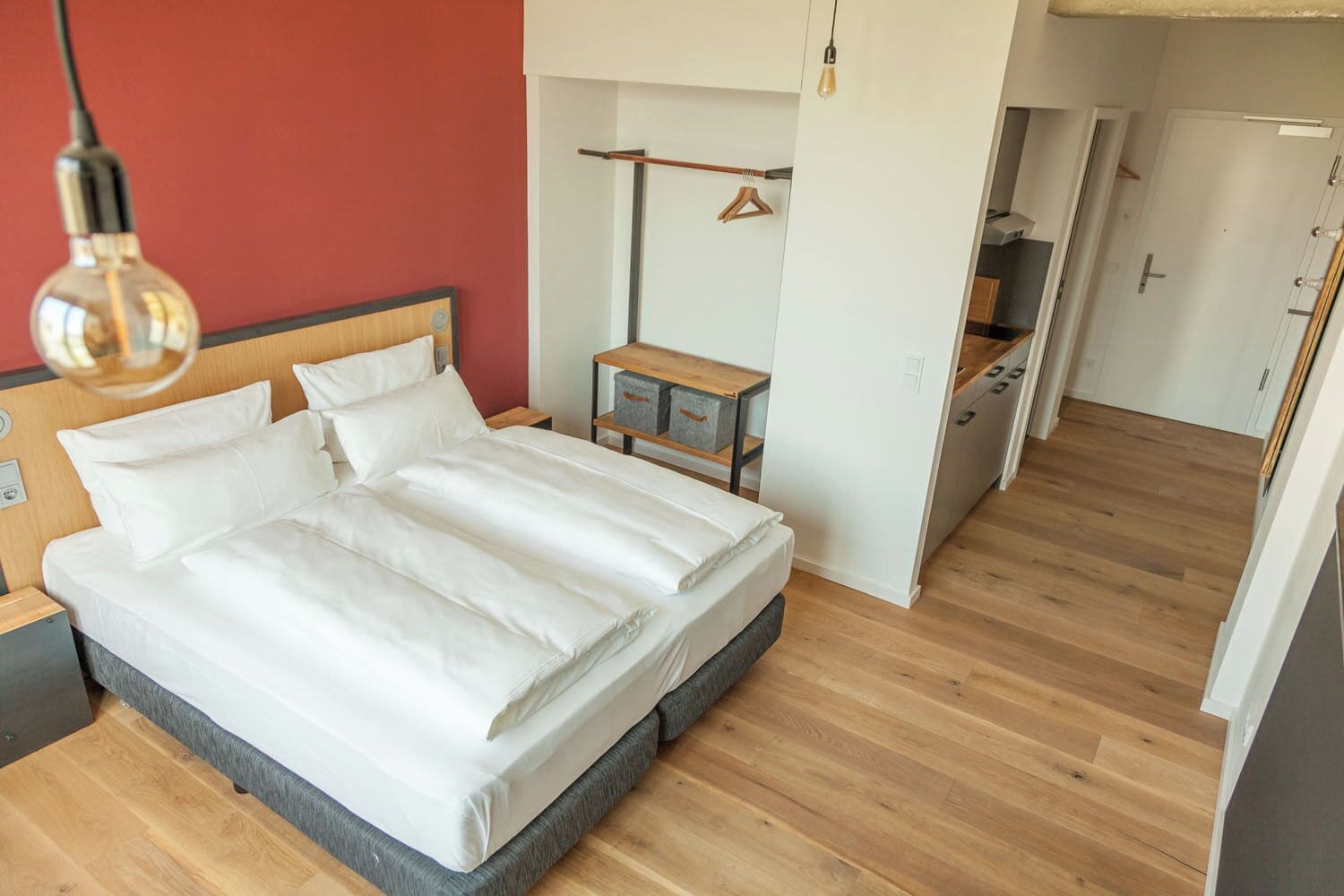 A modern bedroom with a large bed, wooden floor, and a small bedside table with a lamp.