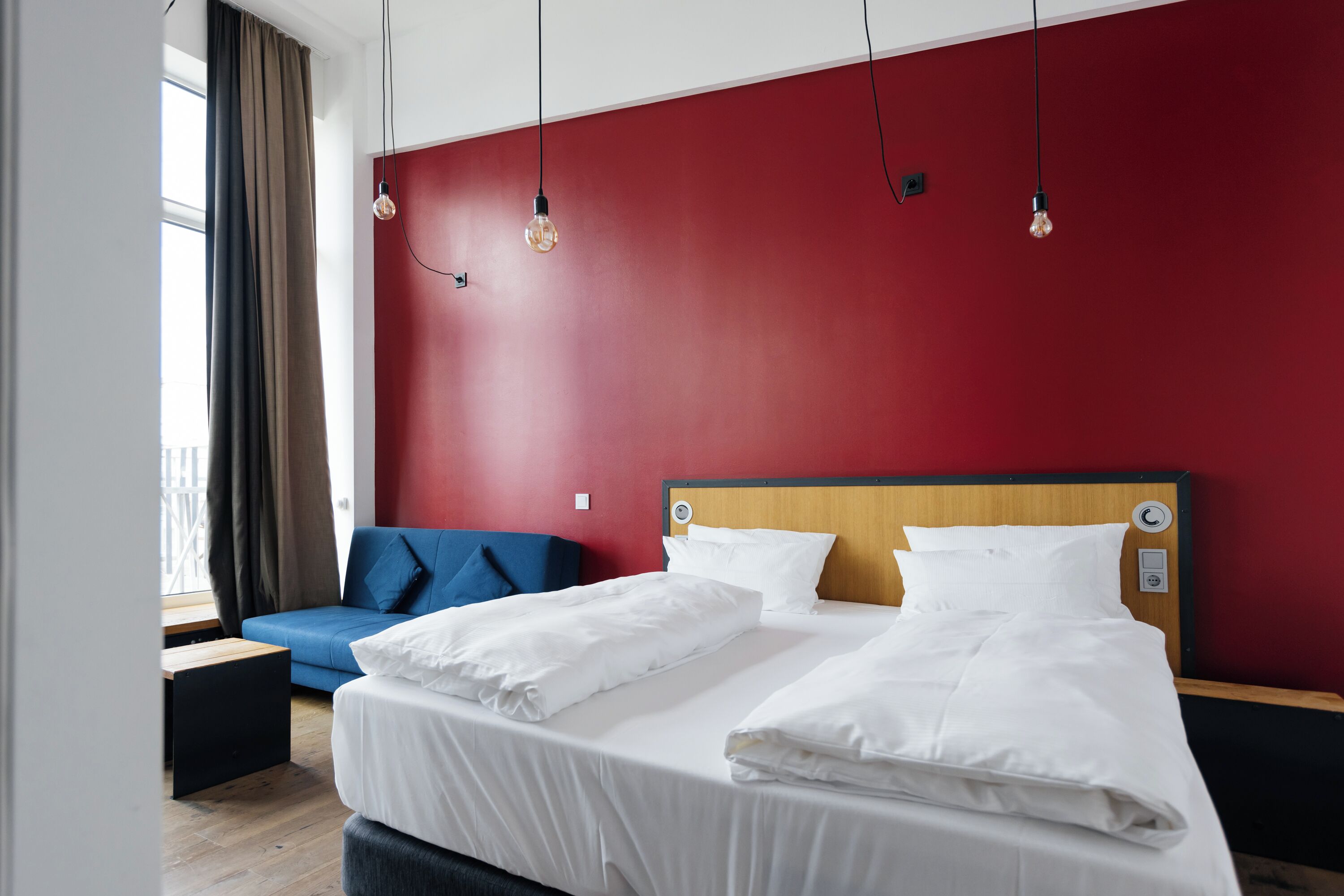 A hotel room with a bed, a blue sofa, a wooden headboard, and a red wall.