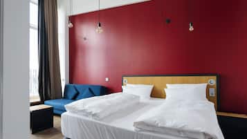 A hotel room with a bed, a blue sofa, a wooden headboard, and a red wall.