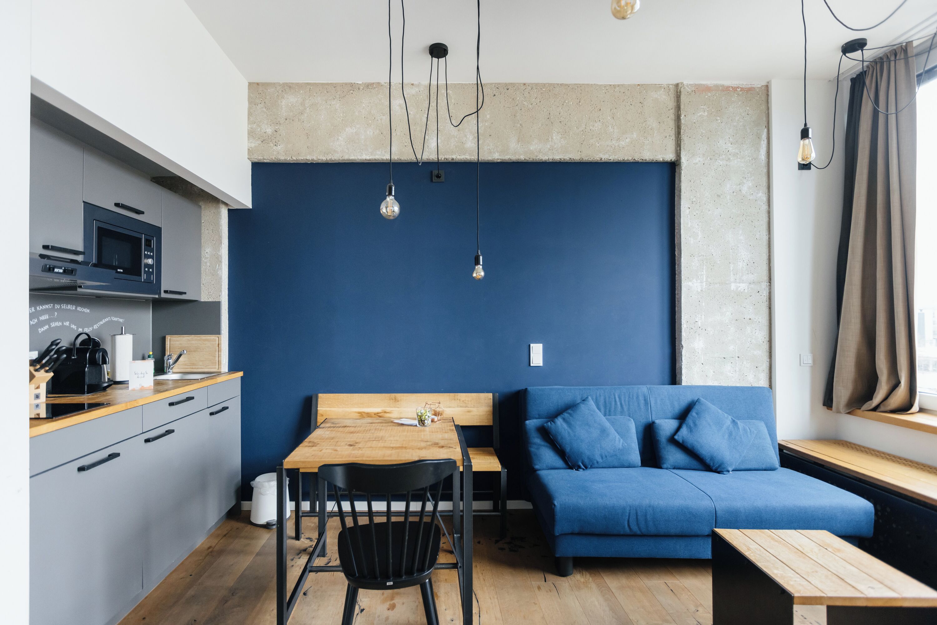 A modern kitchen with a microwave, wooden countertop, and a dining area with a blue sofa and a wooden table.