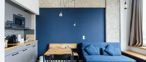A modern kitchen with a microwave, wooden countertop, and a dining area with a blue sofa and a wooden table.