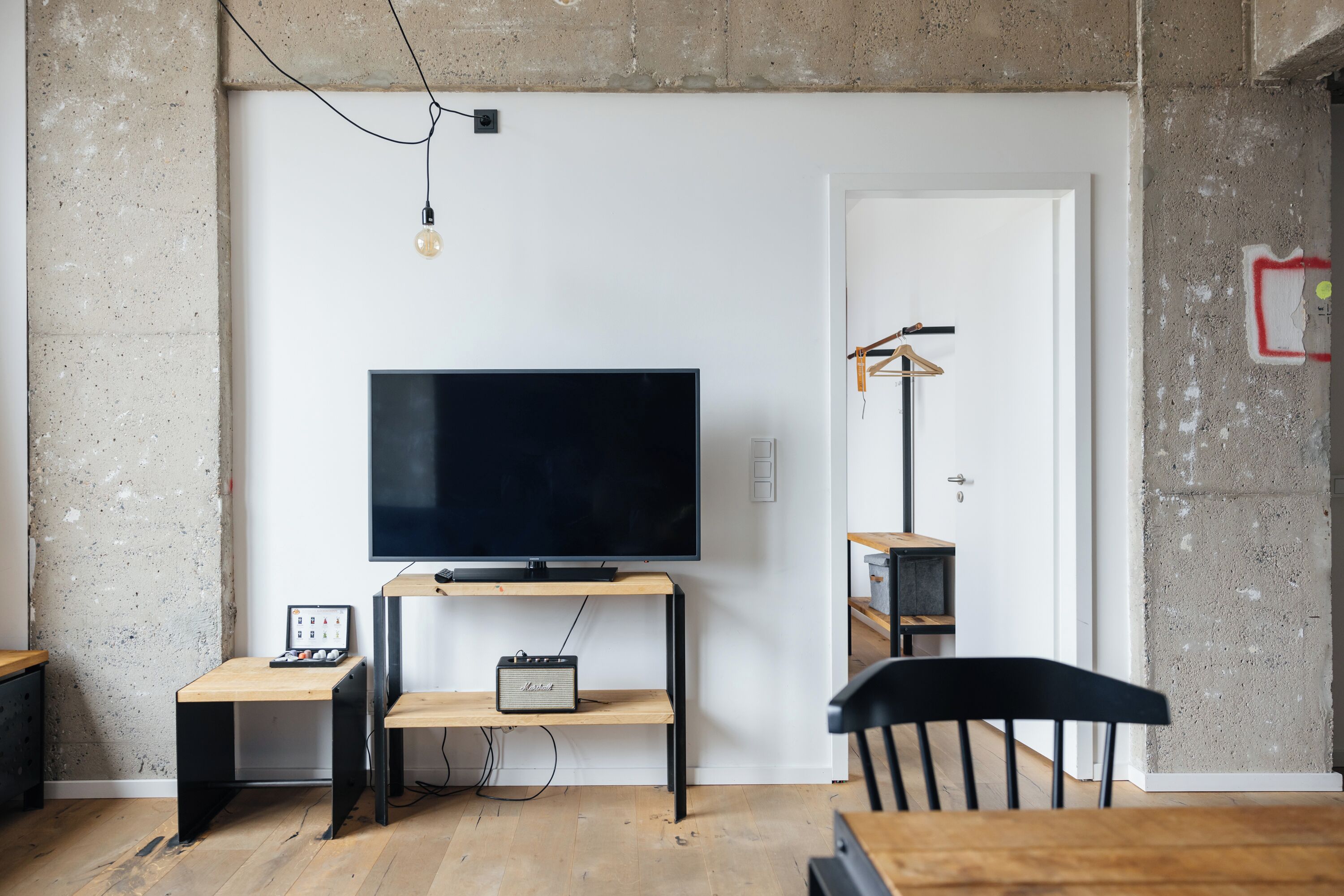 A modern living room with a flat-screen TV, wooden furniture, and exposed concrete walls.
