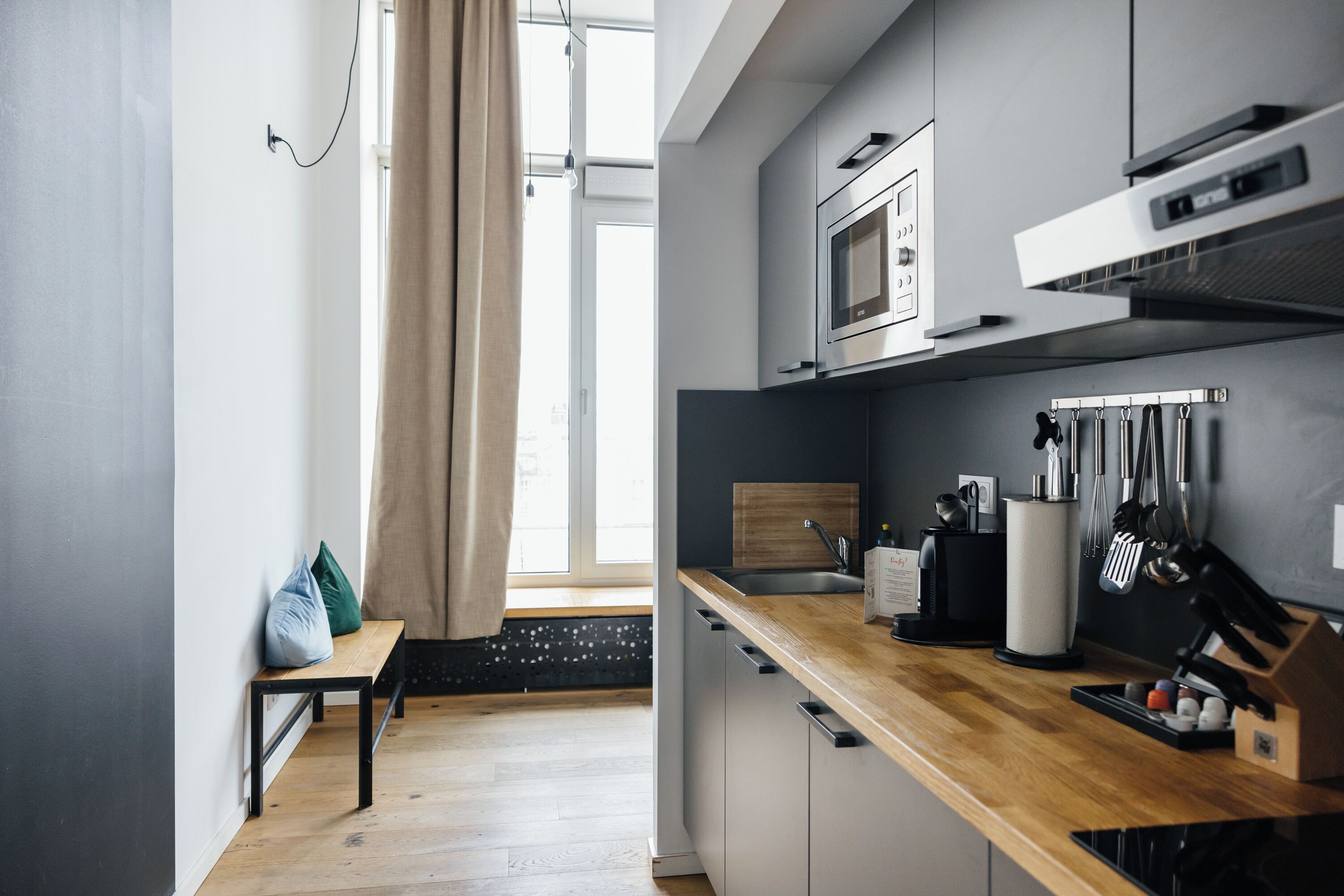 A modern kitchen with a wooden countertop, stainless steel appliances, and a window with curtains.