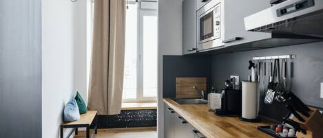 A modern kitchen with a wooden countertop, stainless steel appliances, and a window with curtains.