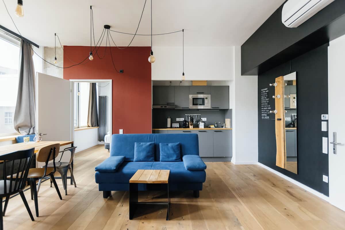 Un espacio habitable moderno con un sofá azul, una mesa de centro de madera y una zona de cocina con microondas.