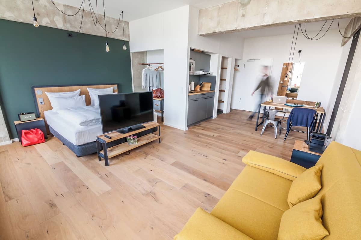 Una sala moderna con un televisor grande sobre un mueble de madera, un sofá amarillo y un comedor con mesa y sillas.