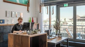 Ein Büro mit Schreibtisch, Computer und Blick auf ein historisches Gebäude durch große Fenster.