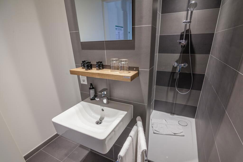 A modern bathroom with a white sink, a shower, and a mirror.