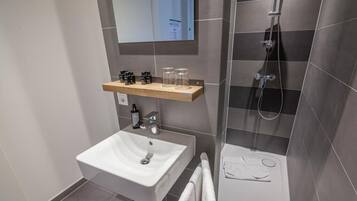 A modern bathroom with a white sink, a shower, and a mirror.