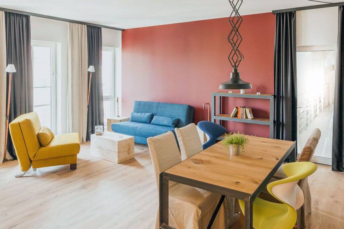 A modern living room with a wooden dining table, yellow and blue sofas, and a bookshelf.