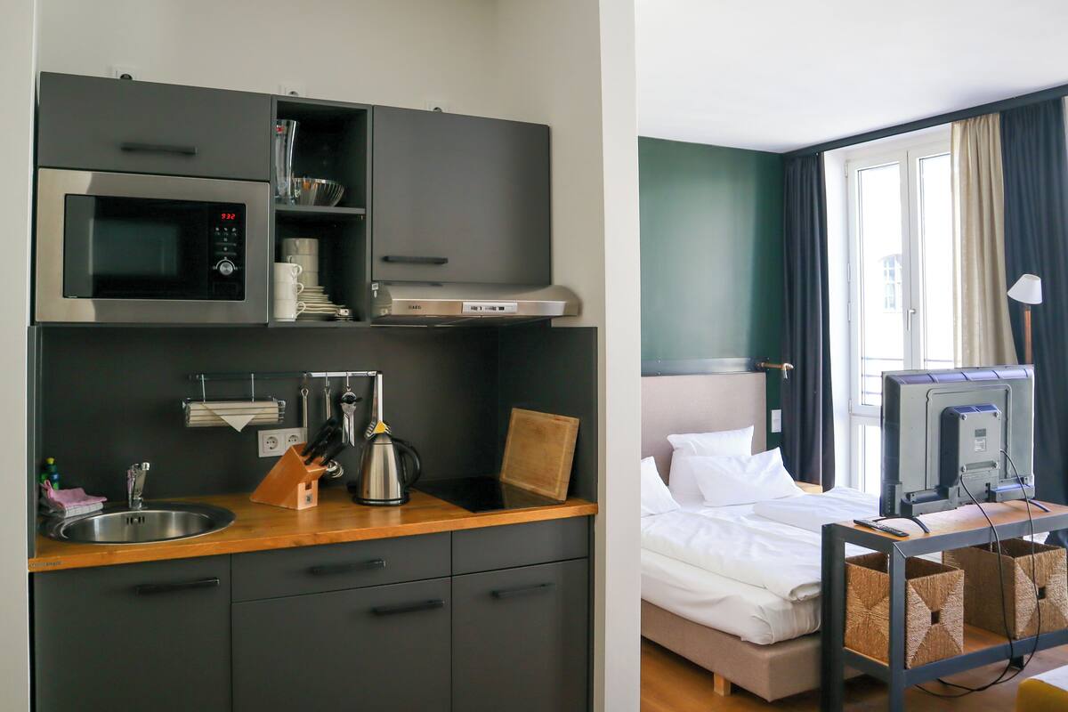 A compact hotel room with a kitchenette, a bed, and a television.