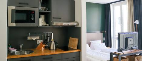 A compact hotel room with a kitchenette, a bed, and a television.
