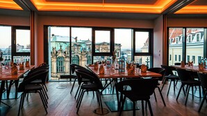 Ein Restaurant mit Blick auf historische Gebäude, Holztische und schwarze Stühle.