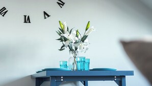 A room with a wall clock displaying Roman numerals, a vase with flowers, and a blue table with glasses. - Vibe Apartment 4, Lord Street (Blackpool)