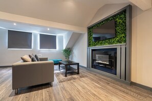Ein modernes Wohnzimmer mit einem grauen Sofa, einem kleinen Tisch und einem Kamin an einer grünen Wand.