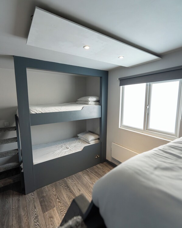 Dormitorio con literas, ventana, suelo de madera y lámpara en el techo.