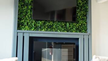 Una sala de estar moderna con una televisión de pantalla plana sobre la chimenea, rodeada de follaje verde.
