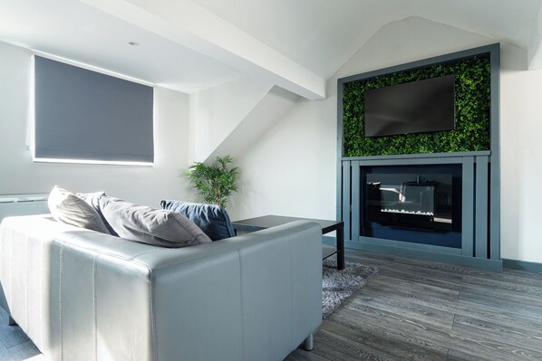 A modern living room with a white sofa, a flat-screen TV mounted on a green wall, and a fireplace.