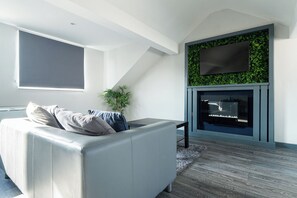 A modern living room with a white sofa, a flat-screen TV mounted on a green wall, and a fireplace.