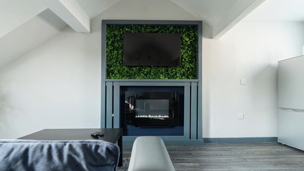A modern living room with a flat-screen TV mounted above a fireplace, a grey sofa, and a wooden floor. - Vibe Apartment 4, Lord Street (Blackpool)