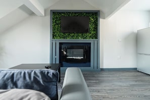 Un salon moderne avec un téléviseur à écran plat fixé au-dessus d’une cheminée, un canapé gris et un plancher en bois.