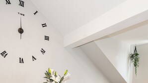 A dining area with a clock on the wall, a table set with plates and glasses, a bench, and a hanging plant. - Vibe Apartment 4, Lord Street (Blackpool)