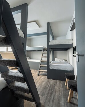 A compact room with bunk beds, a wooden staircase, and a small stool.