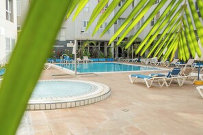 An indoor swimming pool with lounge chairs and a tiled floor, surrounded by a building with windows and plants. - Home2Book Sunny Getaway & Pool in Gáldar (Gáldar)