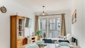 Un comedor con una mesa dispuesta para cuatro, un aparador de madera, un televisor y vistas al exterior a través de amplias ventanas.