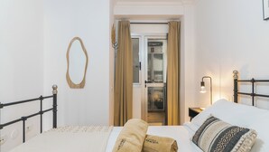 Una habitación de hotel con cama, espejo, puerta con cortinas y mesita de noche con lámpara.
