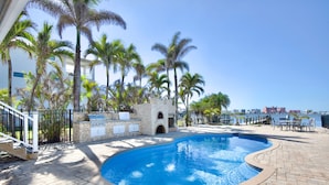 A swimming pool with a curved edge, surrounded by palm trees and a stone wall.