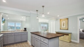 A modern kitchen with grey cabinets, a wooden island, pendant lighting, and a view through the window.