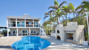 Une maison à deux étages avec une piscine, une cheminée en pierre et des palmiers.
