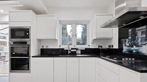 Een moderne keuken met witte kastjes, een zwart aanrecht, een ingebouwde oven, een magnetron en een groot raam.
