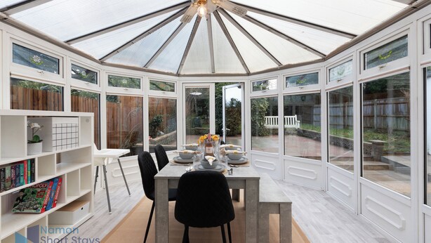 A conservatory with a dining table set for four, surrounded by bookshelves and chairs. - Comfy 4 Bedroom house, Ideal for Workers and Families, FREE Parking (Coulsdon)