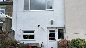 A two-story house with a white exterior, a front door with a small window, and a wooden table and chairs outside. - 2bed Cottage - Trawden - Pet Friendly - Sleeps4 (Colne)