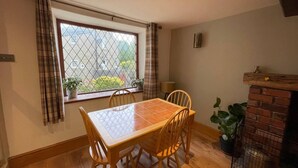 A dining area with a wooden table and chairs, a window with a view of buildings, a brick fireplace, and a potted plant. - 2bed Cottage - Trawden - Pet Friendly - Sleeps4 (Colne)