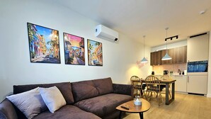 A modern living room with a brown sofa, a dining table with chairs, and a kitchen area with wooden cabinets and a built-in oven. - Apartament Buena Vista - 365PAM (Kolobrzeg)