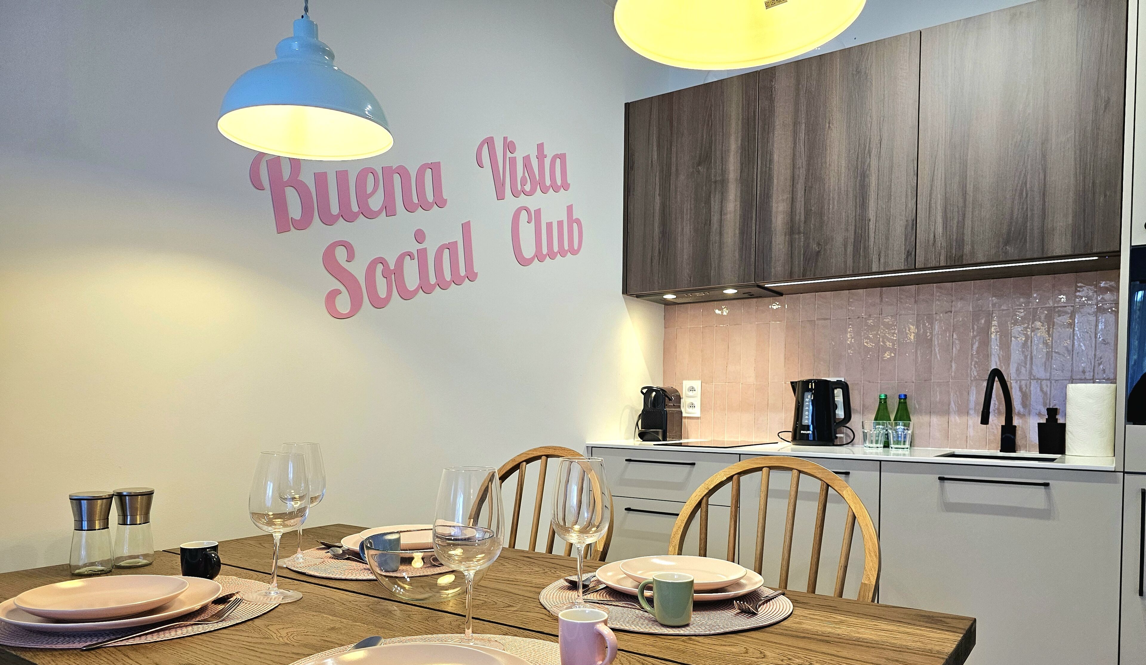 Ein Essbereich mit einem Tisch für vier Personen, eine Küche im Hintergrund und ein Wandschild mit der Aufschrift "Buena Vista Social Club".