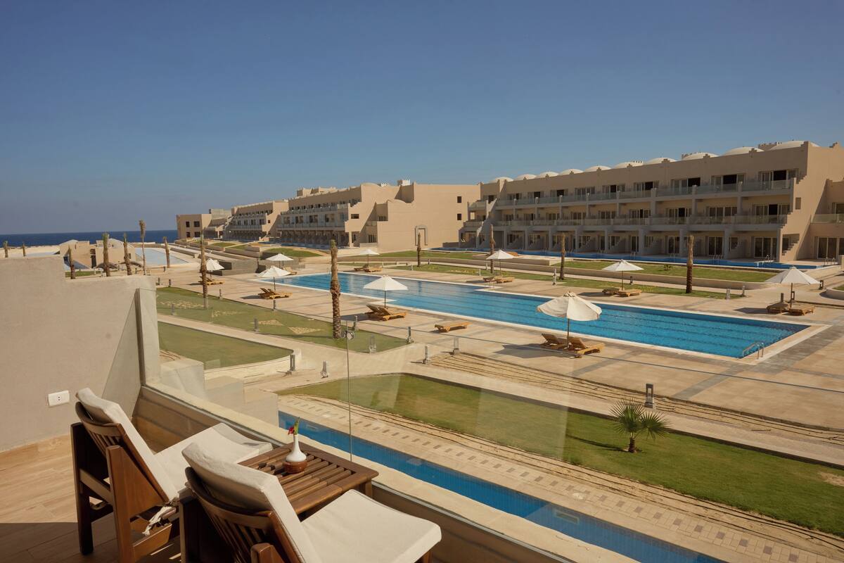 Ein Poolbereich eines Resorts mit Liegestühlen und Sonnenschirmen, einem großen Pool und Blick auf den Ozean.