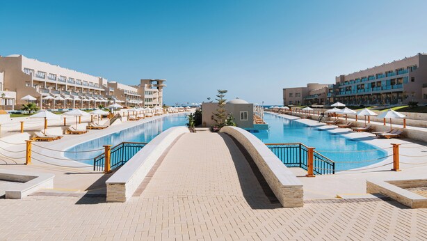 A resort pool area with a clear view of the pool, lounge chairs, and a building with multiple balconies. - Diamond Beach (El Quseir)