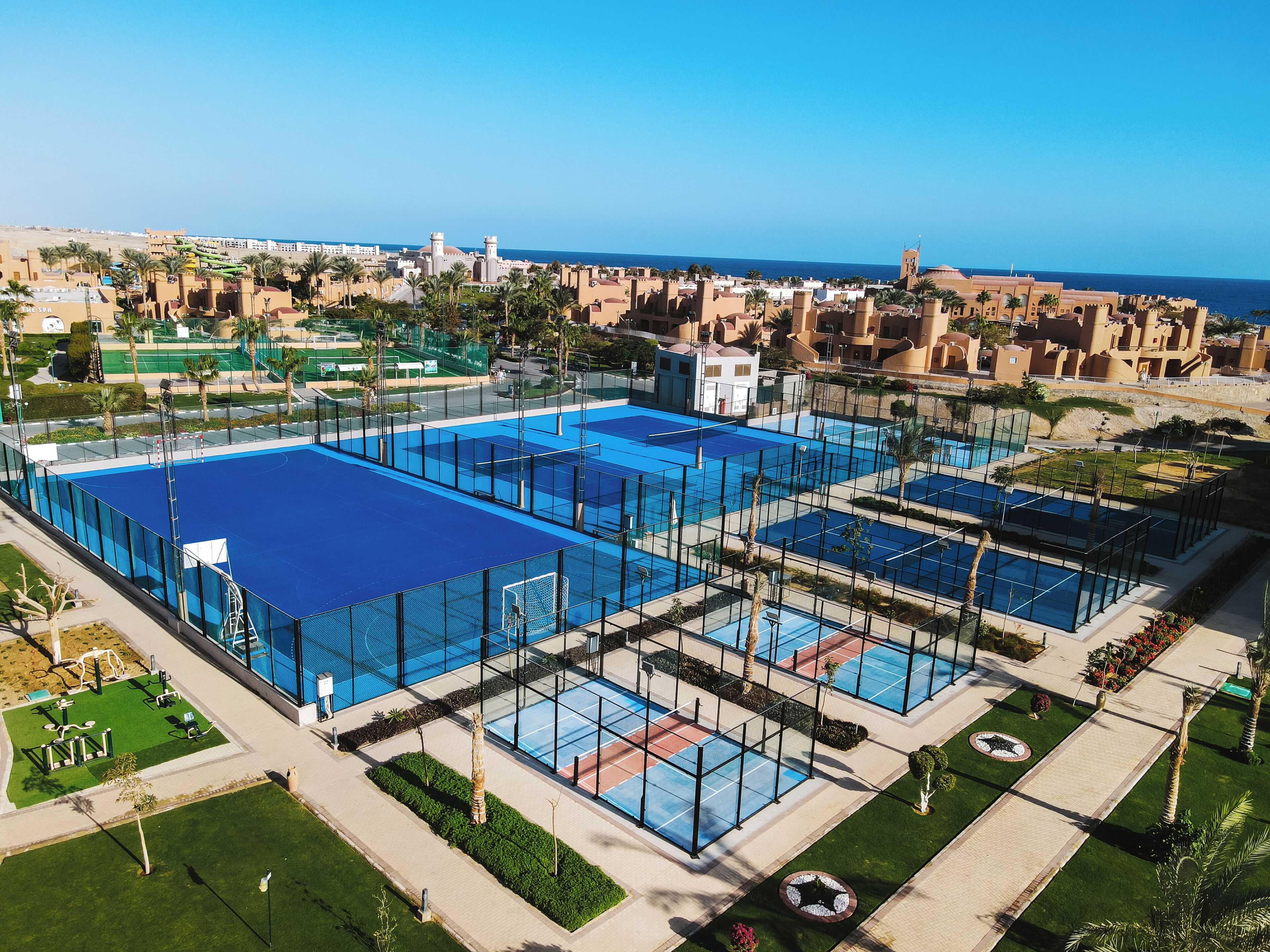 Luchtbeeld van een resort met meerdere zwembaden, palmbomen en een verre uitzicht op zee.