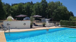 A clear blue swimming pool with lounge chairs and umbrellas, surrounded by a white wall and greenery.