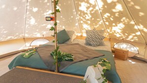 A tented accommodation with a bed, pillows, a small plant, and a wooden box.