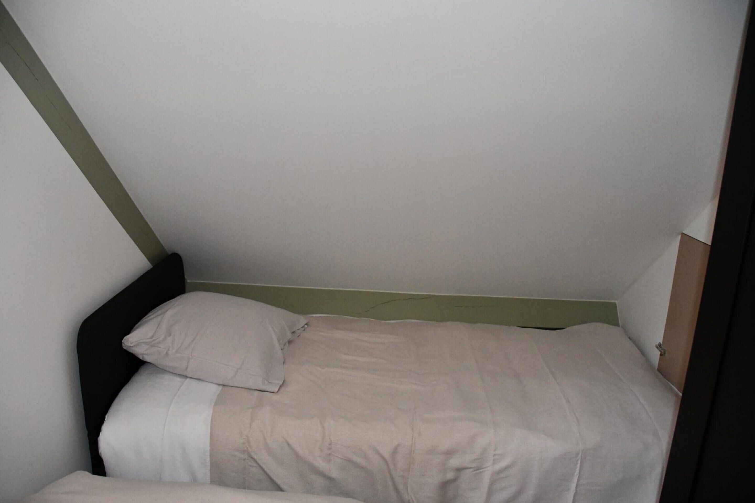 A small, single-bed room with a simple design, featuring a green headboard and a plain white wall.