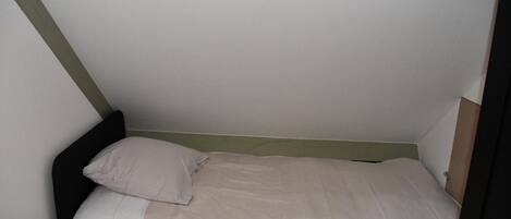 A small, single-bed room with a simple design, featuring a green headboard and a plain white wall.