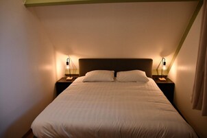 Una cama bien hecha con dos almohadas, flanqueada por dos mesitas de noche con lámparas, en una habitación de diseño sencillo y limpio.